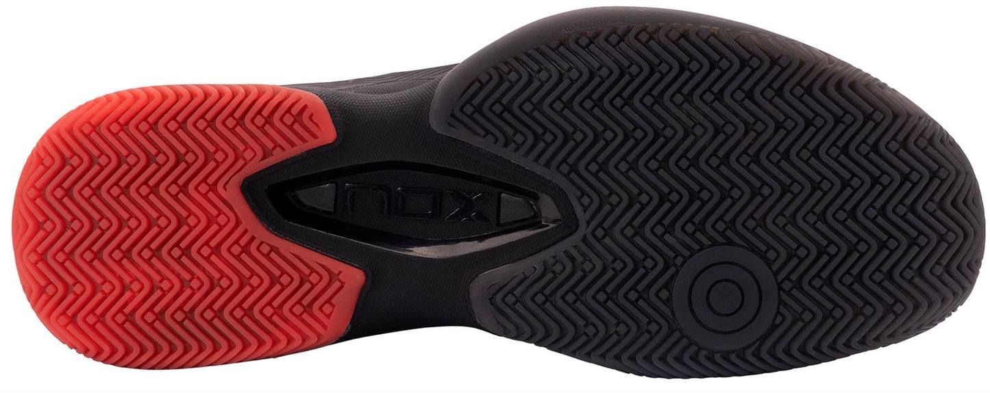 The image shows the sole of the NOX AT10 Lux Men's Padel Shoes by NOX, featuring a black and red rubber grip with a herringbone pattern—details chosen by Agustin Tapia for top performance on the padel court.