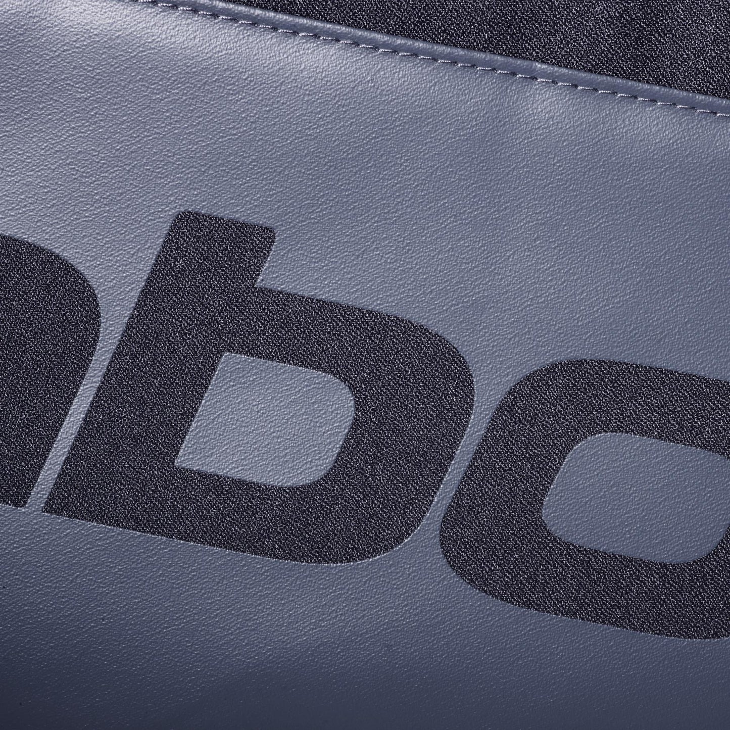 Close-up of textured gray material from the Babolat Court S Padel Racket Bag - Black, featuring a bold black lowercase "b"—showing only part of the text on this Babolat padel equipment.