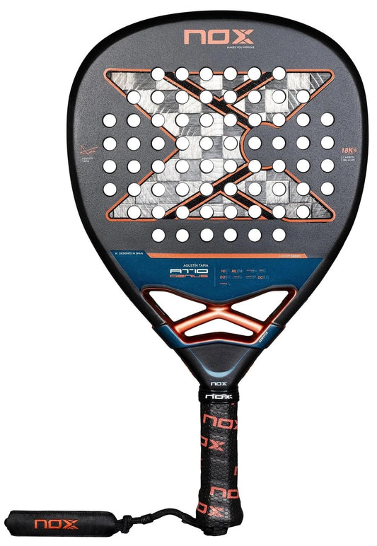 The NOX AT10 Luxury Genius Attack 18K Alum By Agustin Tapia 2025 padel racket features a black design with orange accents, a textured surface with holes, an "X" center motif, and a black and orange grip with a matching wrist strap.
