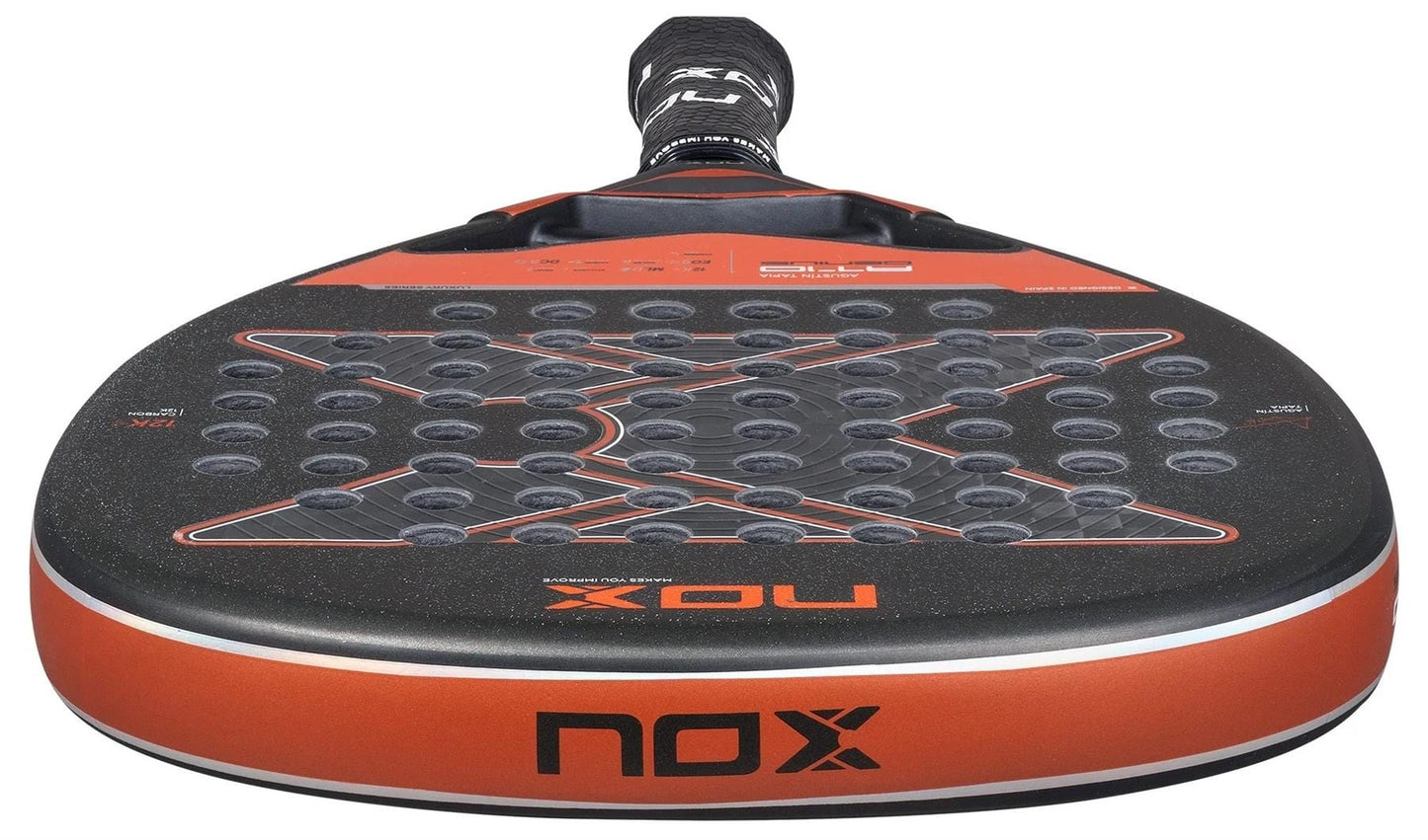 Close-up of the NOX AT10 Luxury Genius Attack 12K By Agustin Tapia 2025 padel racket, showing its black and orange design, large X pattern, perforated face, and premium 12K carbon fibre construction for top performance.