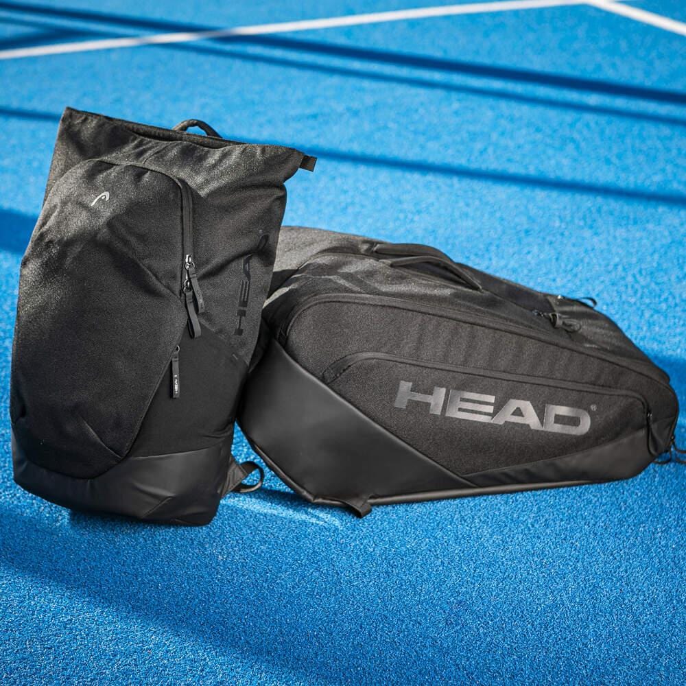 Two HEAD Pro X Padel Backpack 25L - Black by HEAD, with a racket compartment and urban style, rest on a vibrant blue outdoor court marked with white lines in the background.
