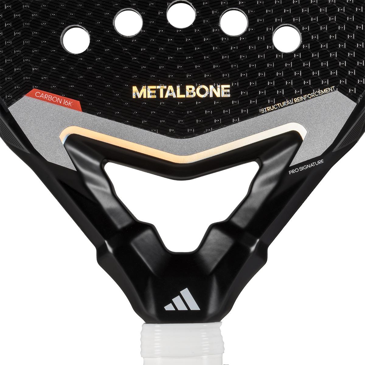 Close-up of the adidas Metalbone 3.4 Padel Racket for advanced players, featuring a gold "METALBONE" text, carbon 16K construction, and structural reinforcement. It includes a white logo at the base and a textured black design with circular holes.
