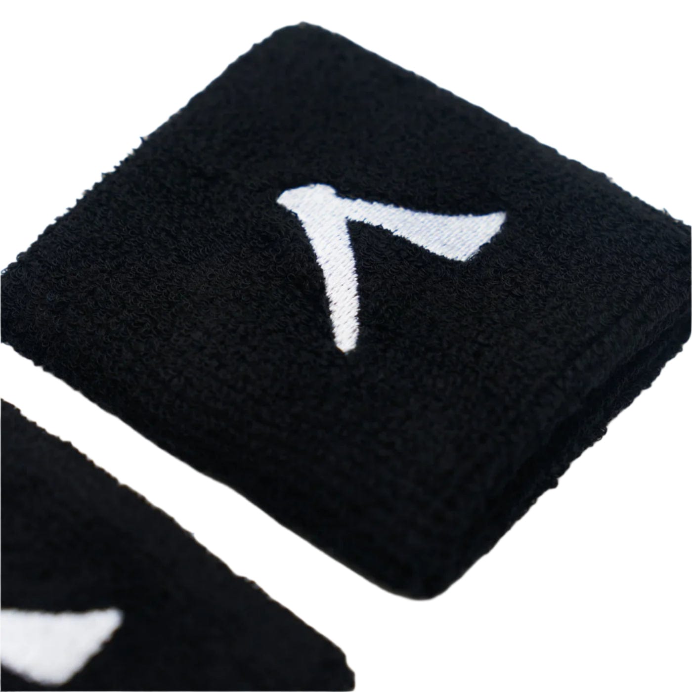 A Kanso 7cm Wristband from the black 2-pack, featuring a white stylized 'A' logo, lies on a white surface. Another wristband is partially visible nearby. Made from absorbent fabric by Kanso, it ensures maximum comfort with its soft texture.