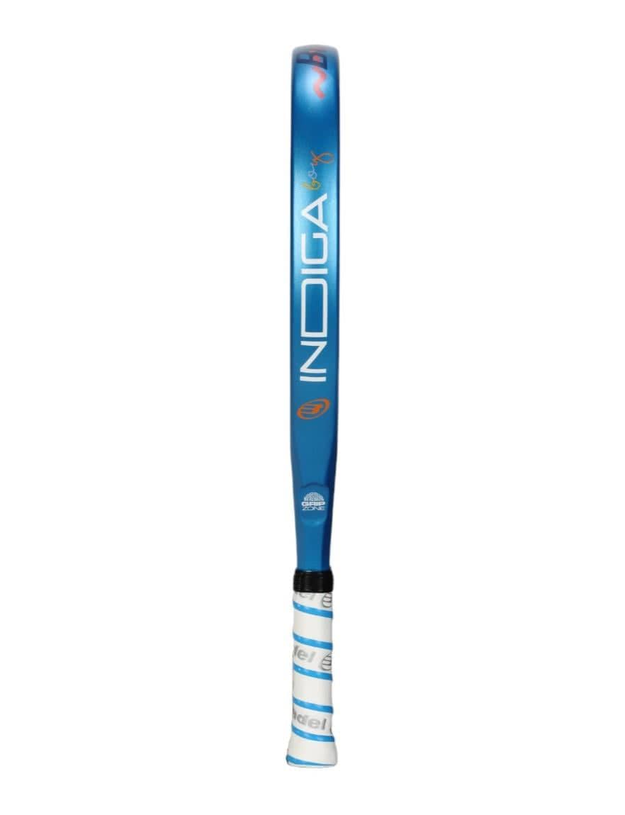 A Bullpadel Indiga Junior 25 Boys Padel Racket in blue and silver stands vertically, showcasing the "Bullpadel" brand. Enhanced with Grip Zone technology, the handle features a stylish wrap of white and blue grip tape for superior control.