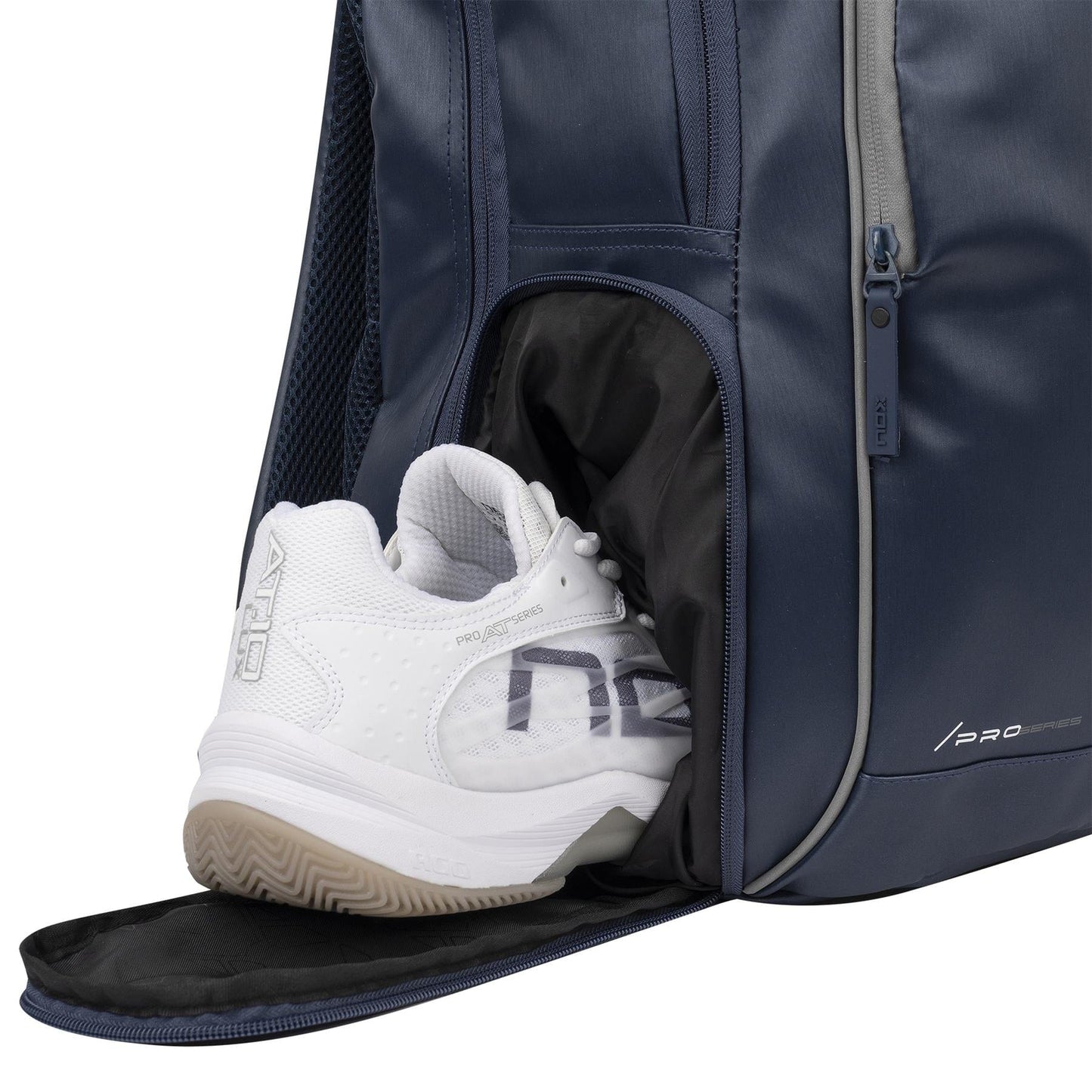 A white athletic shoe is partially tucked inside the NOX Pro Series Padel Backpack - Blue by NOX, with the zippered compartment flap open to reveal shoe details and the integrated air ventilation system.