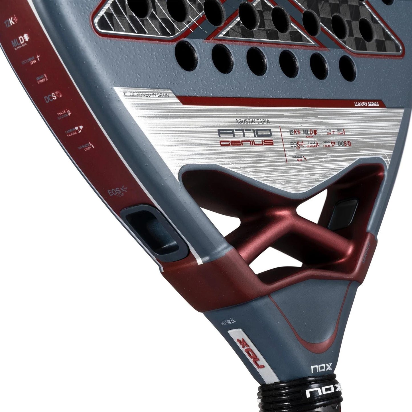 Close-up of the NOX AT10 Luxury Genius 12K By Agustin Tapia 2025 padel racket, showcasing detailed textures, 12K carbon fibre, NOX branding, red/gray/silver accents, visible holes, technical specs, and angular design.