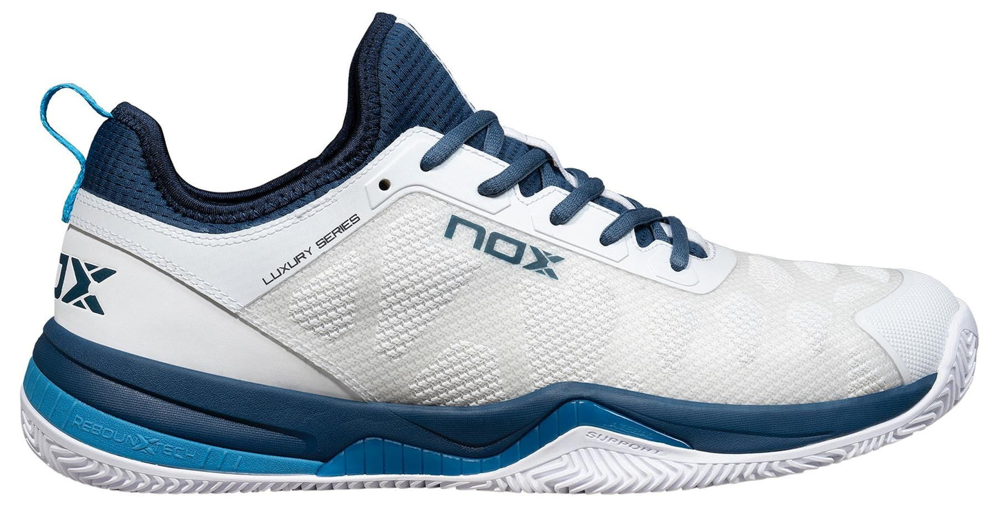 The NOX Nerbo Mens Padel Shoes in White/Swedish Blue feature a mesh upper, blue sole and accents, blue laces, heel pull tab, and "NOX" plus "LUXURY SERIES" text for comfort and performance on court.