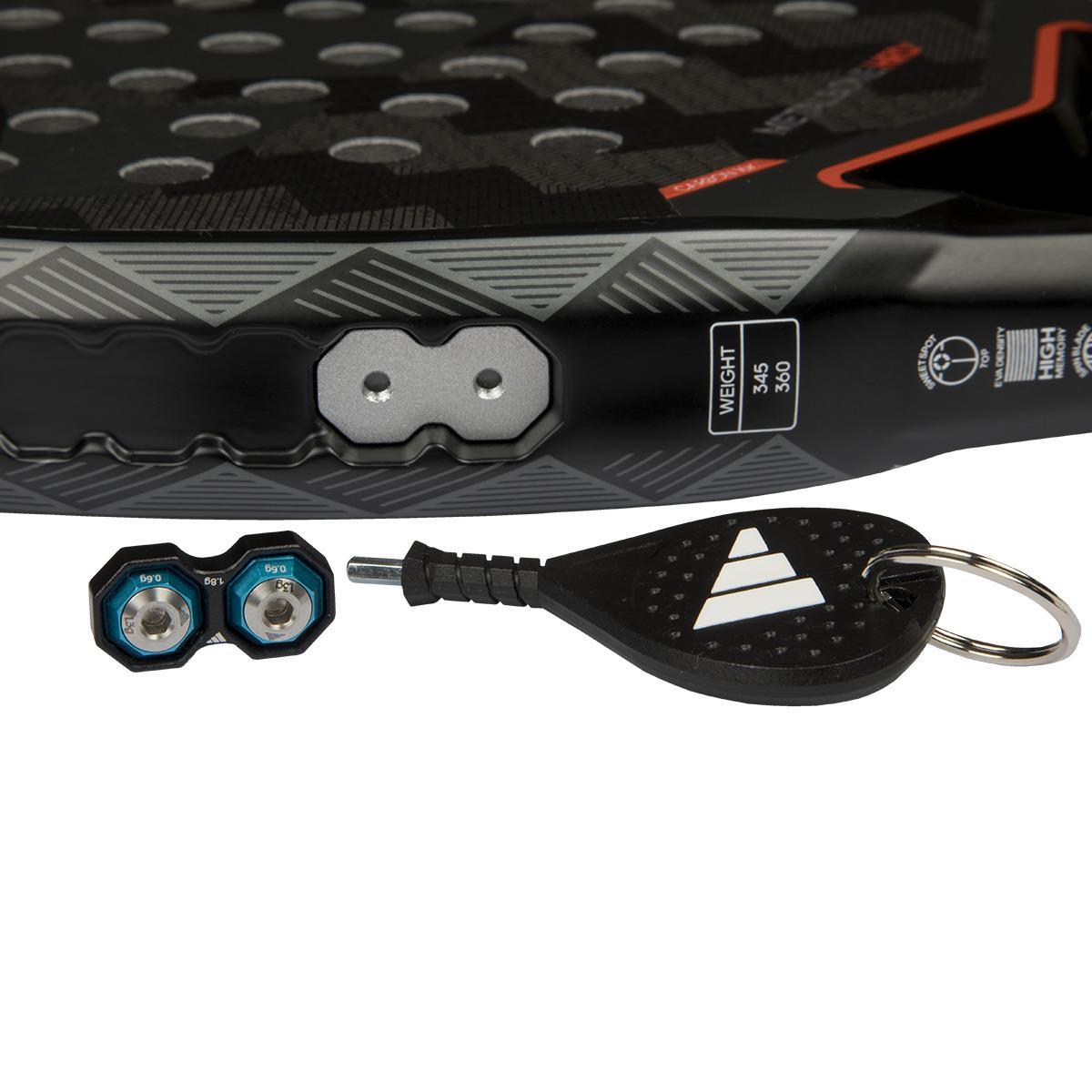 Close-up of the adidas Metalbone 3.4 Padel Racket in black/white, featuring hexagonal patterns, a weight sticker, and tension markings. Designed for advanced players, it includes two metallic weights with blue rims and a black logo keychain tool.