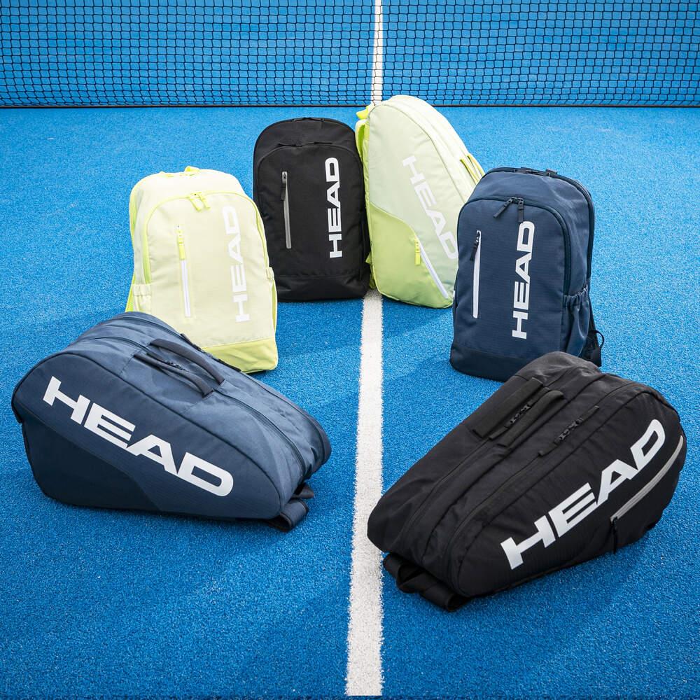Six HEAD BASE Padel Backpack 17L bags in black are arranged in a semicircle on a bright blue tennis court, with the net visible in the background.