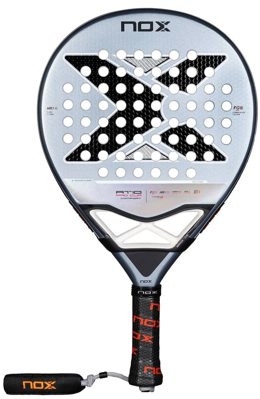 The NOX AT10 Pro Cup Comfort By Agustin Tapia 2025 Padel Racket features a bold large “X” design, circular holes, black grip with red accents, Smartstrap® wrist strap on the handle, and sleek silver, black, and red details.