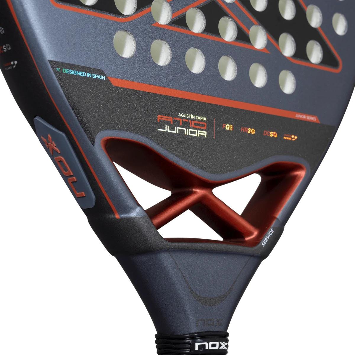 Close-up of the NOX AT10 Genius Junior by Augustin Tapia 2025 padel racket, featuring a textured surface with circular holes and red-black accents, inspired by the AT10 Luxury Genius design—perfect for young players.
