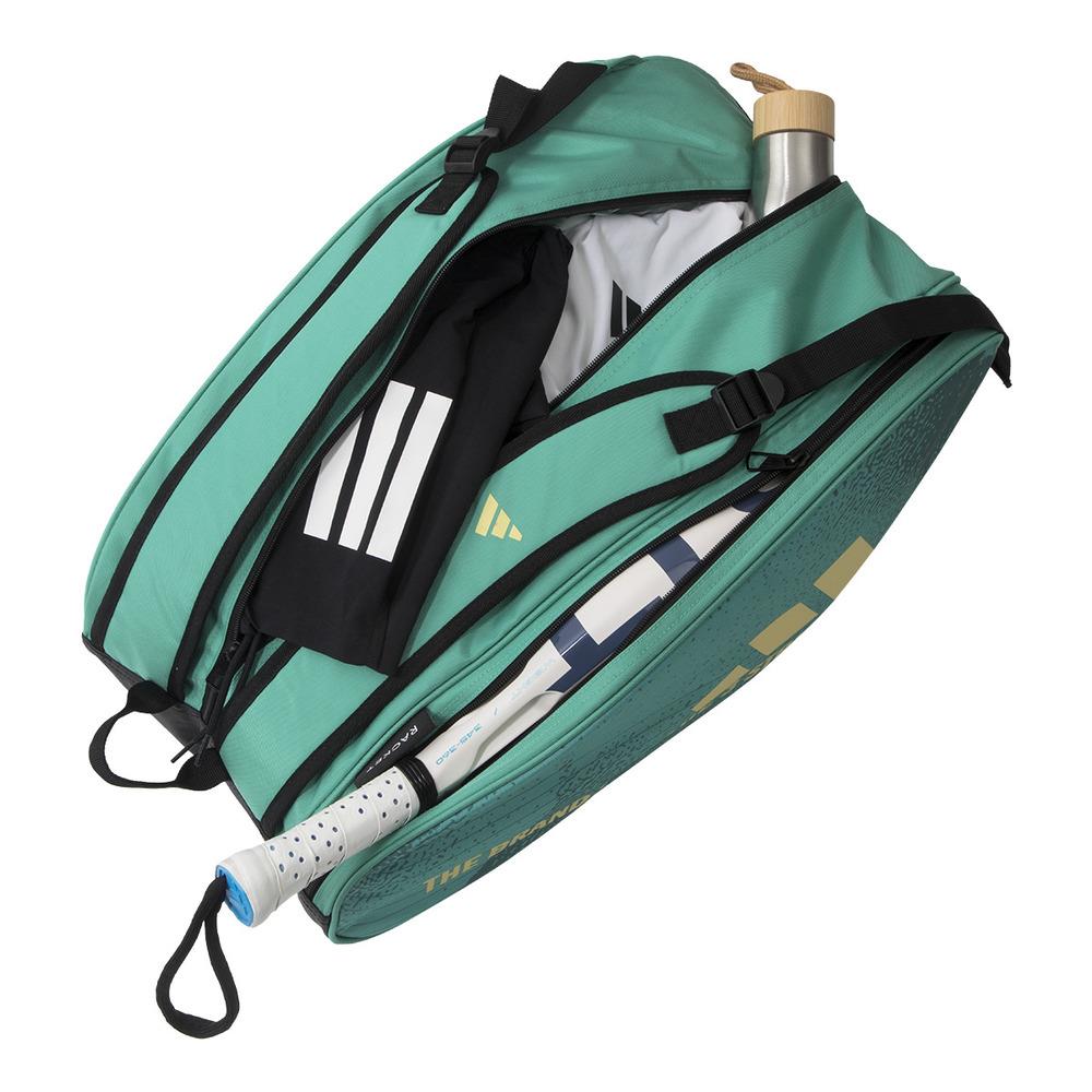 The ADIDAS Control 3.4 Padel Racket Bag - Green is open, revealing a tennis racket, a wooden-capped water bottle, and a black and white sports towel. Designed for court accessories, it features multiple compartments and a comfortable shoulder strap.