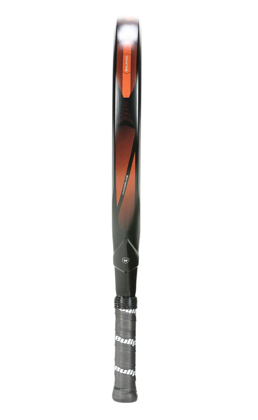 A close-up of a Bullpadel Vertex Junior 25 Padel Racket stands vertically against a white background. The sleek design features a black and red color scheme with a wrapped handle displaying the Bullpadel brand name, ideal for junior players seeking modern style.