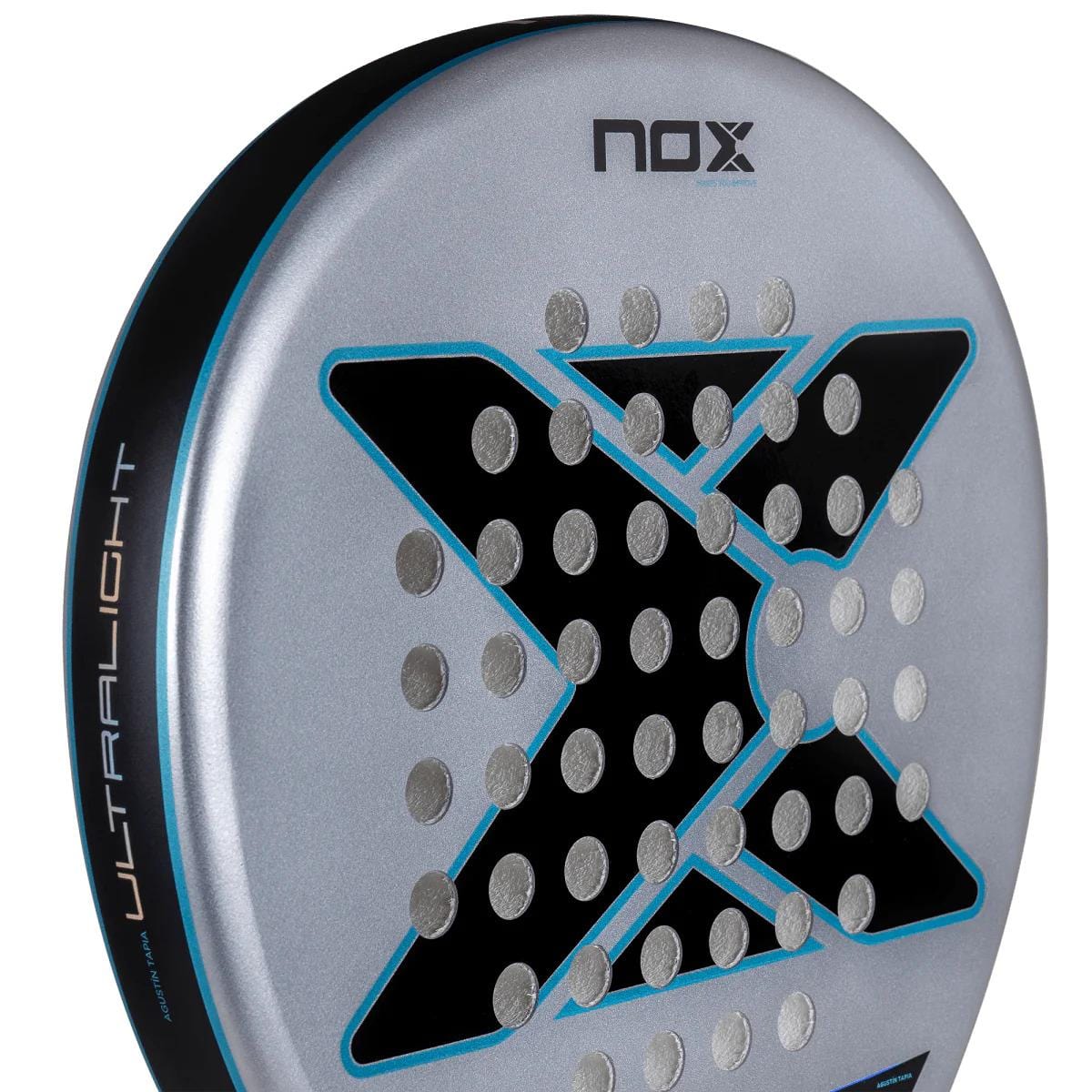 Close-up of the NOX AT10 Genius Ultralight By Augustin Tapia 2025 Padel Racket in Fibre Glass Silver, showing a bold black "X", perforated holes, blue accents, and "Ultralight" text on the side.