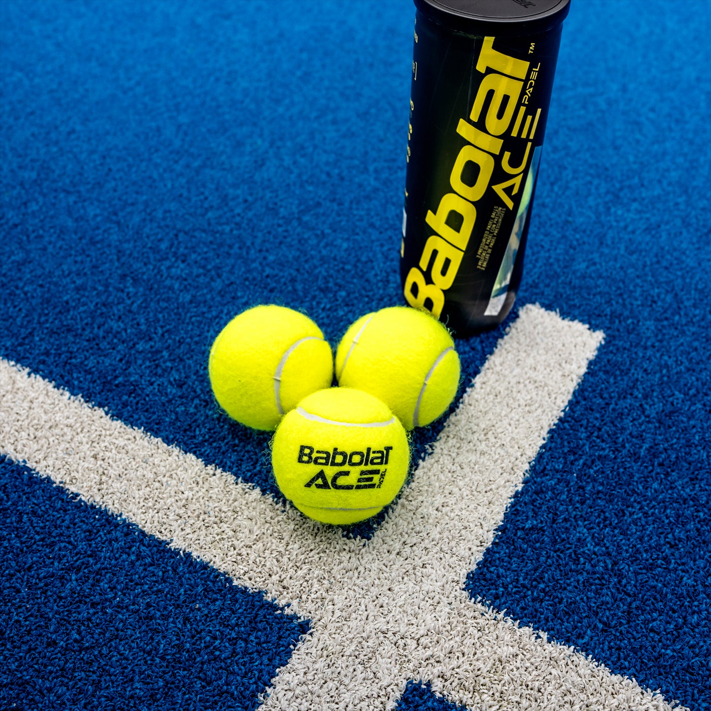 Three yellow Babolat Ace Padel X3 balls lie on a blue court near a black canister with "Babolat Ace" labeling. Positioned on an intersecting white line, the scene embodies the precision championed by the International Padel Federation.