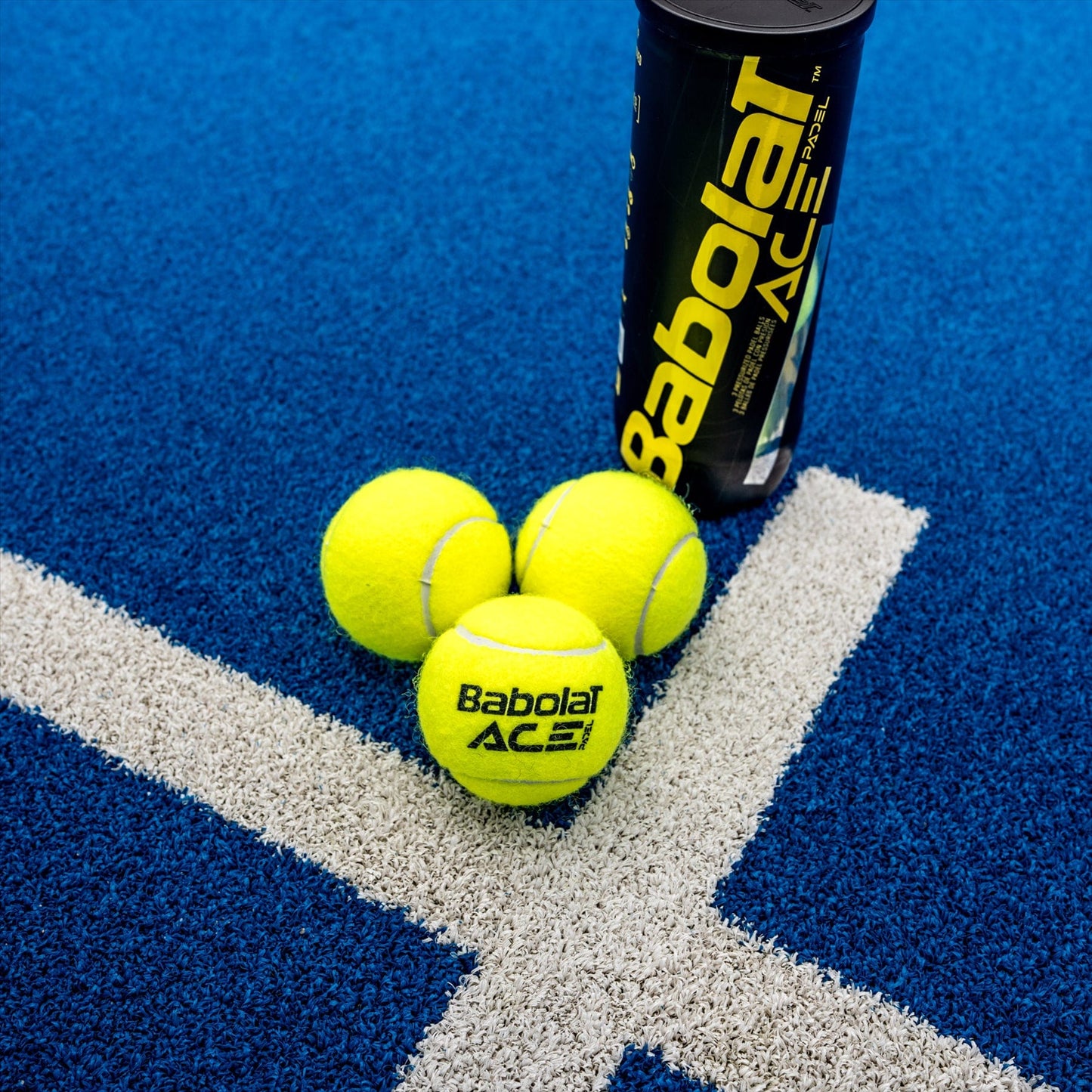 Three yellow Babolat Ace Padel X3 balls lie on a blue court near a black canister with "Babolat Ace" labeling. Positioned on an intersecting white line, the scene embodies the precision championed by the International Padel Federation.