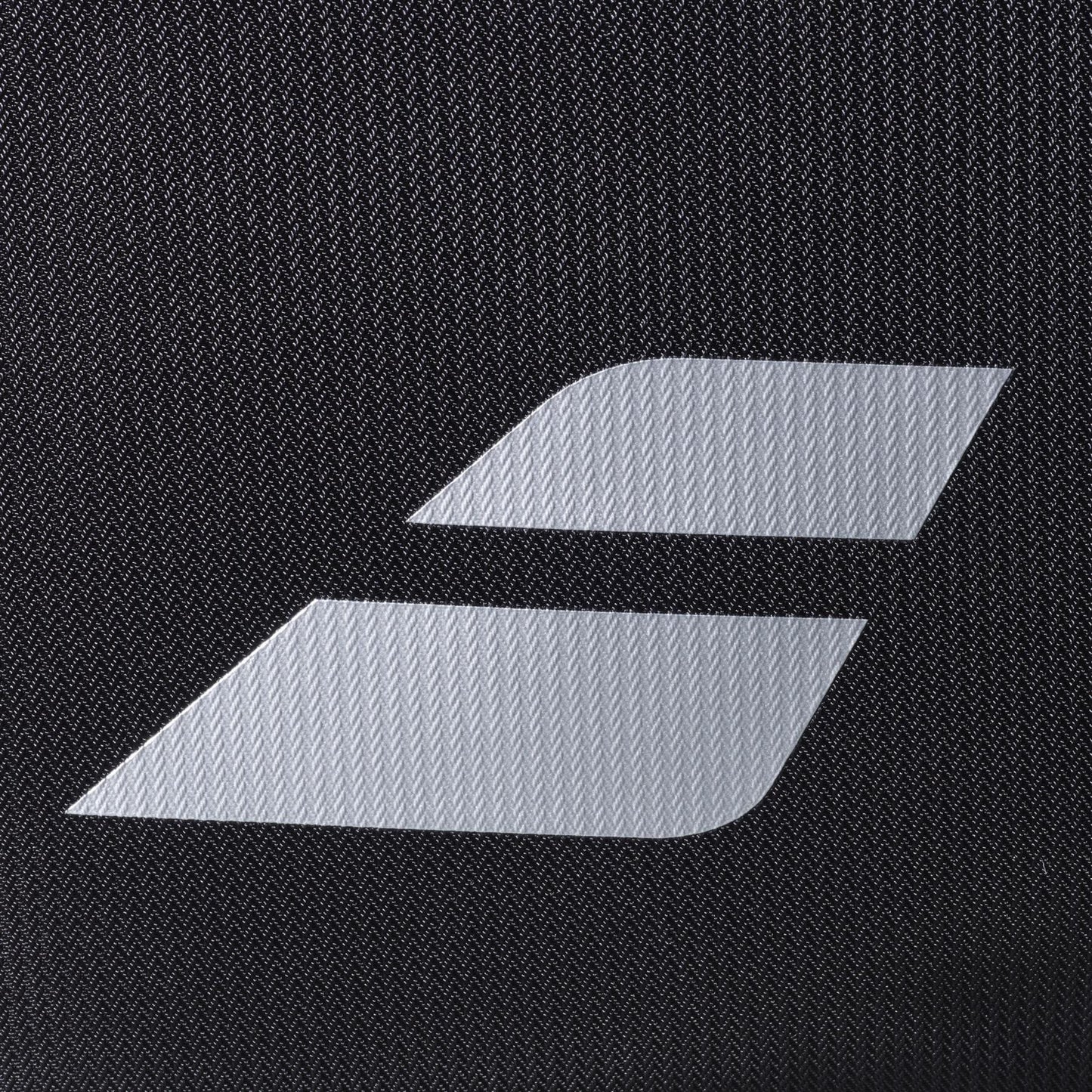 A close-up of the Babolat RH Perf Padel 2nd Gen Backpack in Black/Silver, showing its textured black surface and the white minimalist Babolat logo with two diagonal stripes, echoing its signature high-performance padel bag design.