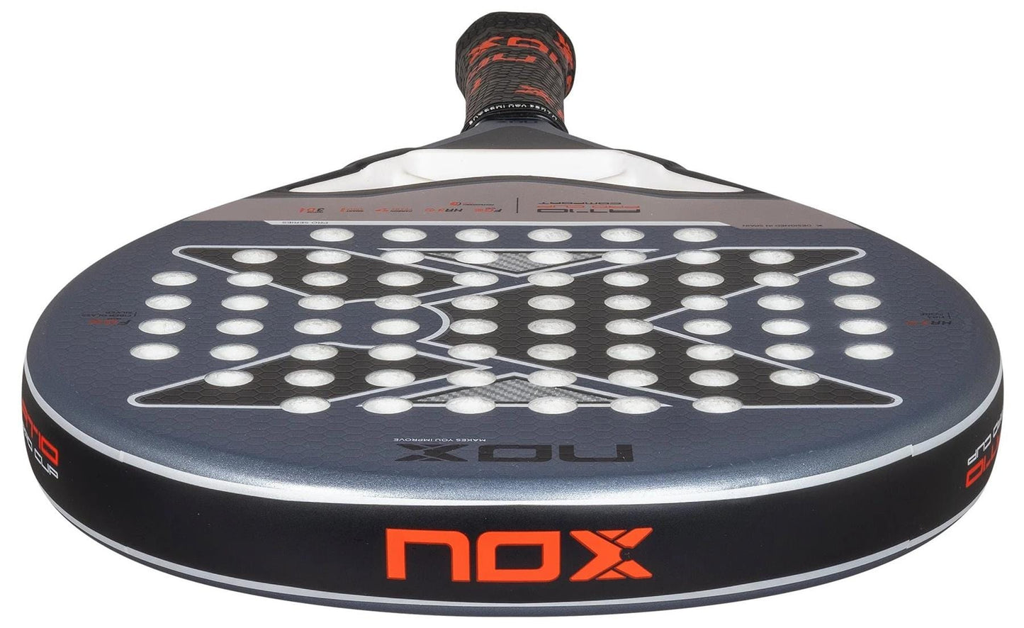 A close-up of the NOX AT10 Pro Cup Comfort By Agustin Tapia 2025 padel racket shows its round head with white holes, black and gray geometric patterns, the orange NOX logo on the edge, and a visible Smartstrap® for safety.