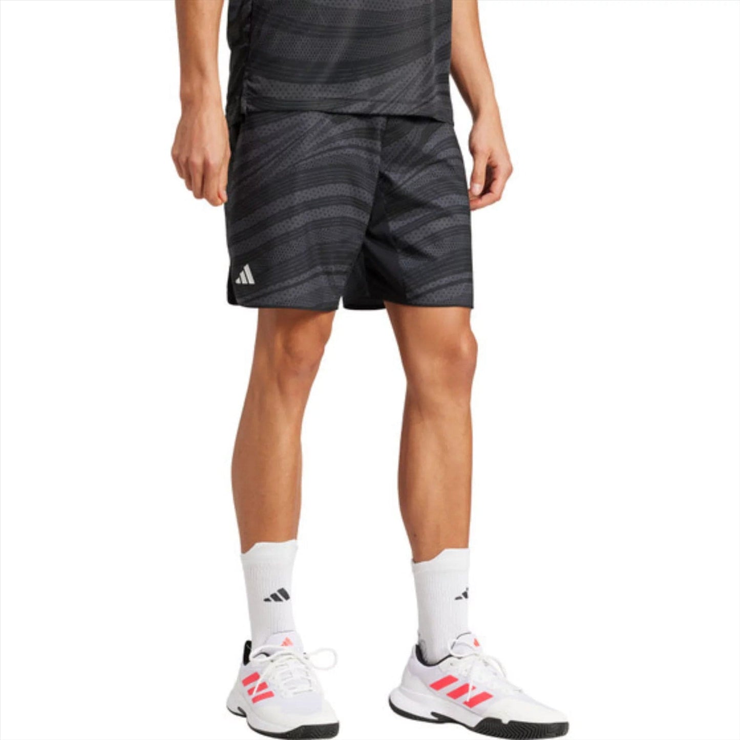 Wearing a black athletic outfit with subtle stripes, the person pairs white socks and white sneakers with pink accents. They might be in ADIDAS Club Graphic Men's Padel Shorts in black, made from recycled materials with AEROREADY tech to stay dry. Part of their face is obscured.