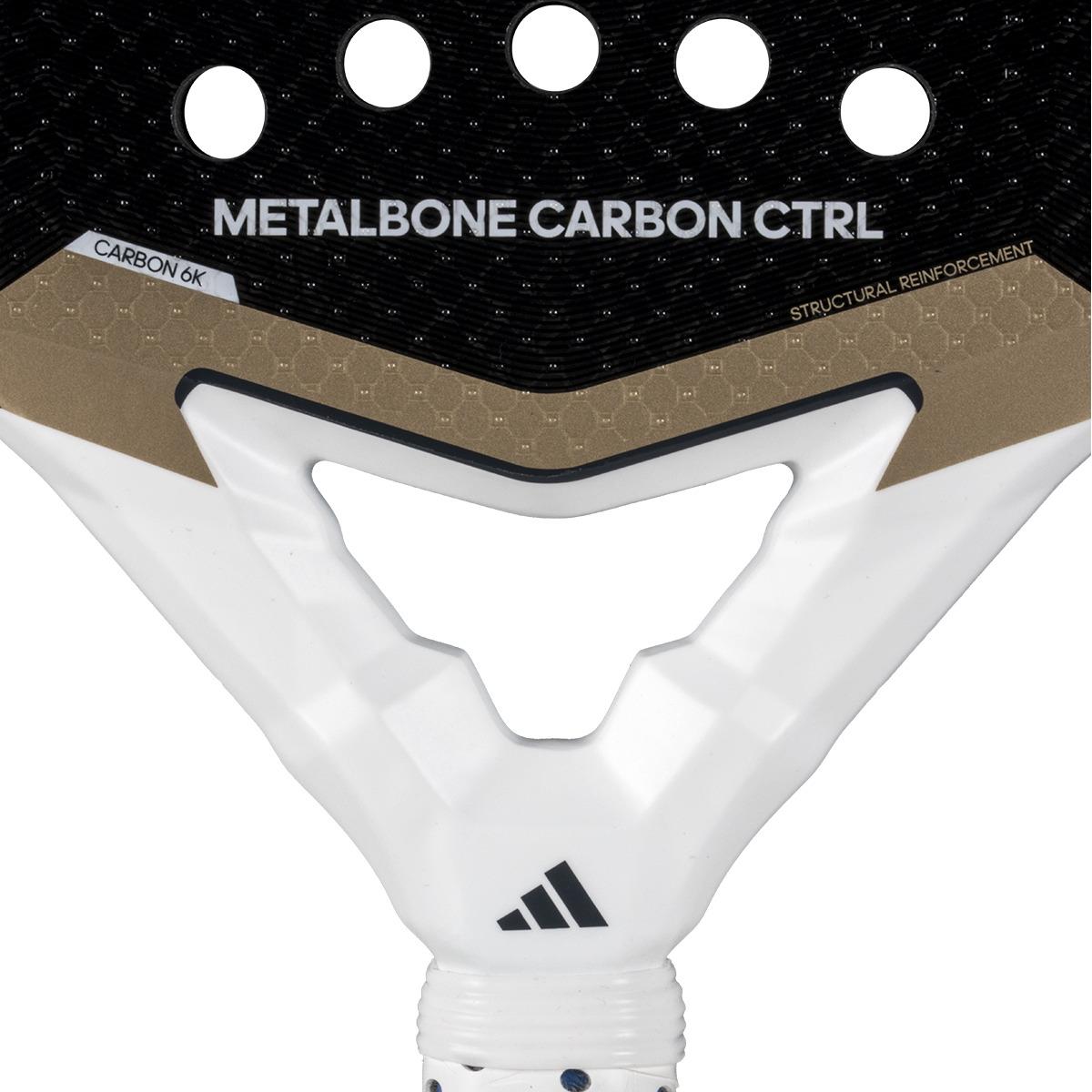 Close-up of the adidas Metalbone Carbon CTRL 3.4 padel racket head, ideal for advanced players, with "METALBONE CARBON CTRL" and "CARBON 6K" text on its black and gold textured surface. A unique hole pattern enhances its sleek white handle.
