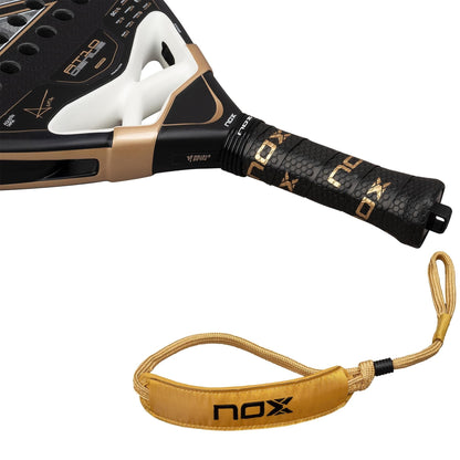 Close-up of the NOX AT10 Genius 18K Alum By Agustín Tapia 2026 Padel Racket handle, wrapped with "NOX" grip tape, showing the Weight Balance system and a gold wrist strap with the NOX logo.