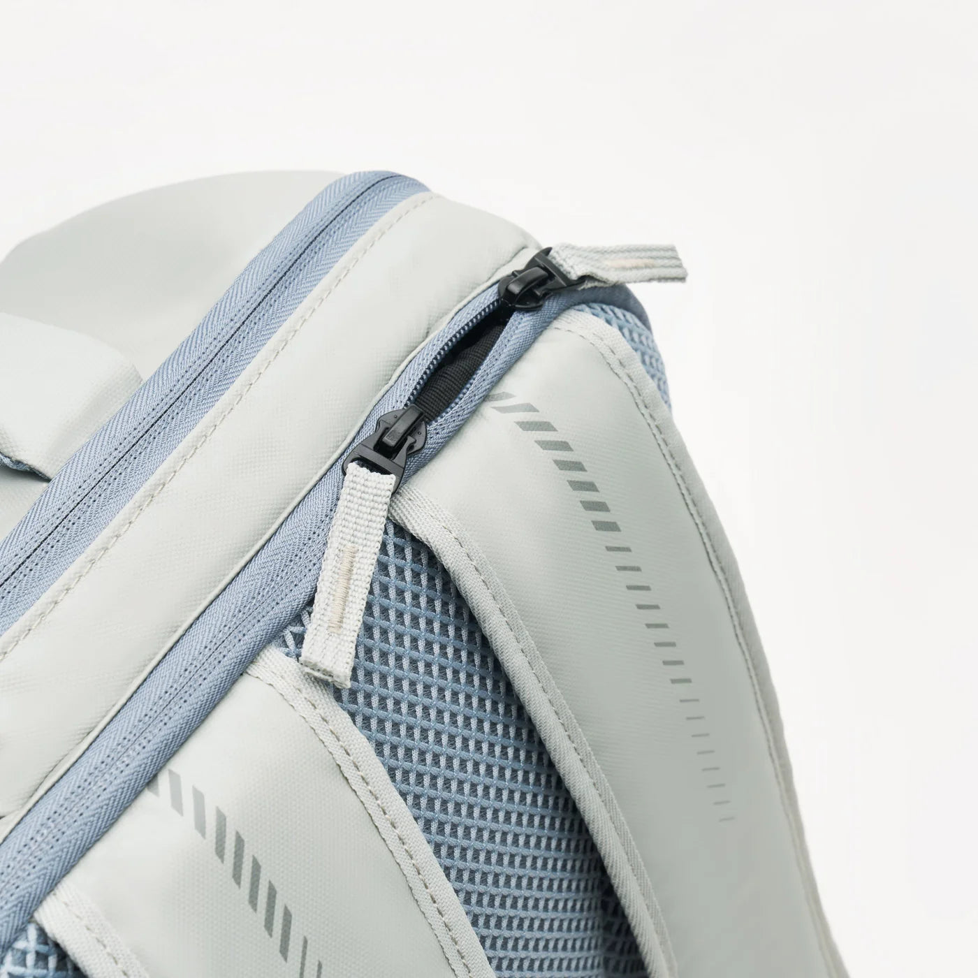 The Kanso Intuko Padel 23L Backpack in grey is shown against a white background with its zipper partially open, revealing its practical design. It features a netted side pocket, striped detailing, and a racket compartment, while the reflective print adds unique flair.