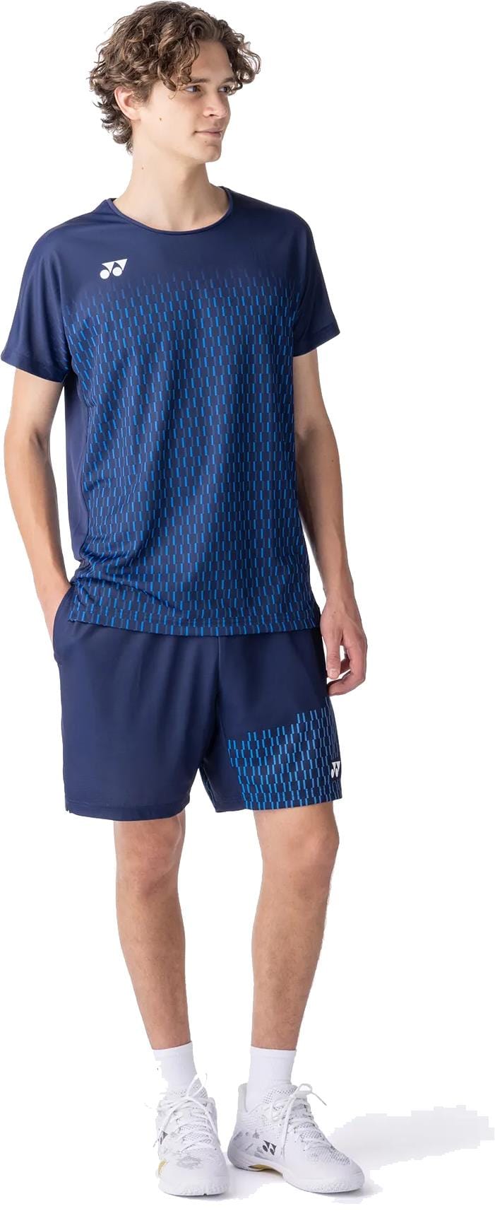 A young man wears the Yonex 10713EX Crew Neck Men's Padel T-Shirt in Dark Navy with matching shorts and white shoes, looking to the side with his hands in his pockets.