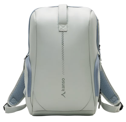 The Kanso Intuko Padel 23L Backpack is a sleek, minimalist design in light gray with blue mesh side pockets and shoulder straps. It features a reflective vertical "kanso" logo and provides a dedicated racket compartment for added functionality.