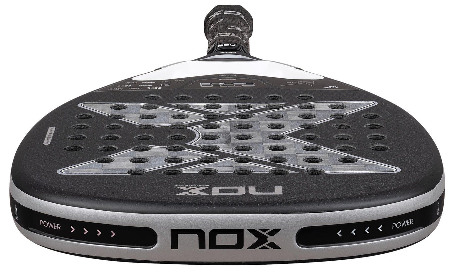 Close-up of the NOX Luxury AT10 Genius Attack 18K Alum By Agustin Tapia 2026 Padel Racket, featuring a black and silver face with a large "X" design, circular perforations, and an 18K aluminised carbon finish.