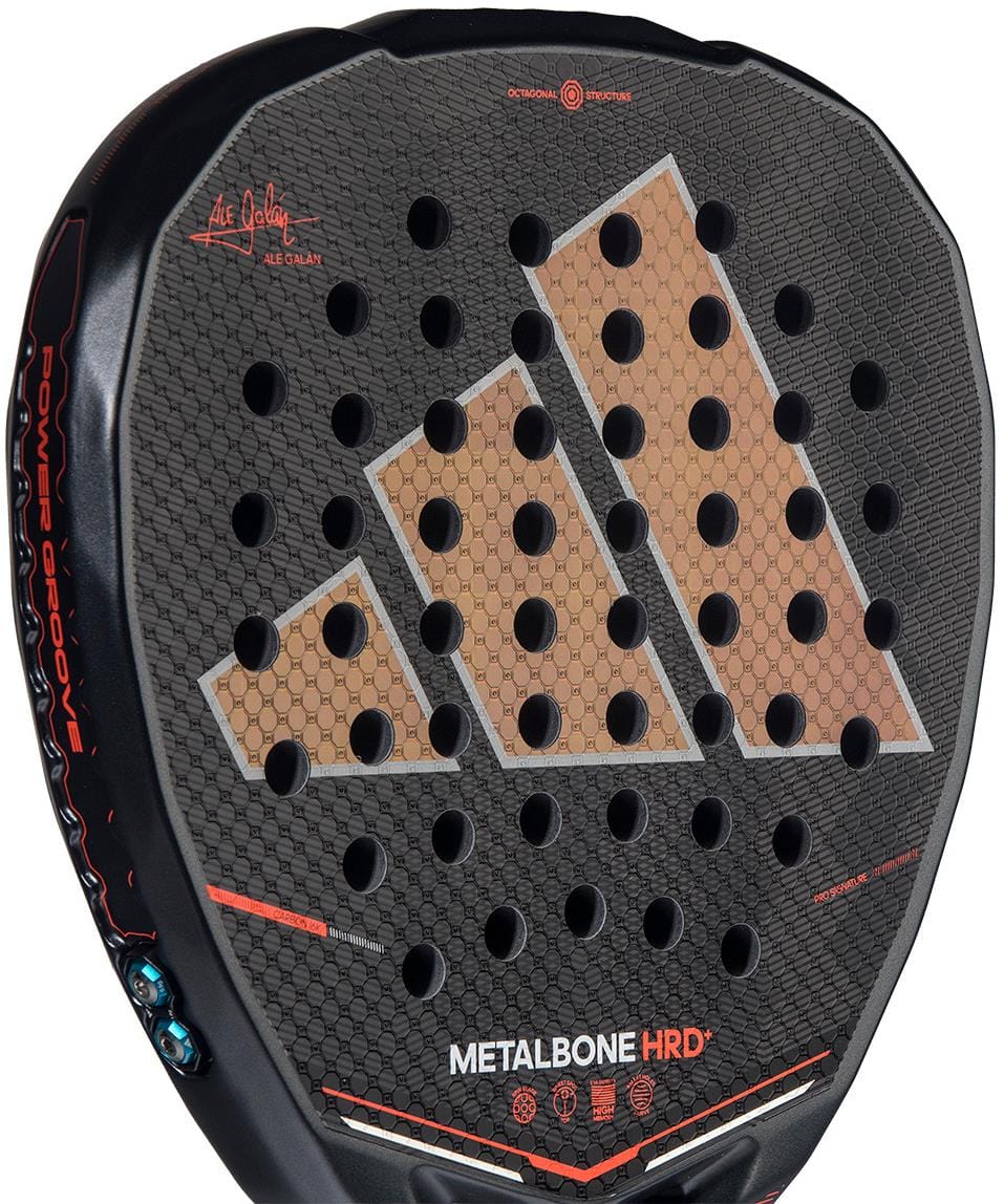 Close-up of the adidas Metalbone HRD+ by Ale Galán 2026 padel racket in black/red, showcasing a honeycomb pattern, circular holes, tan adidas logo, and "METALBONE HRD" text that highlights this advanced power racket’s design.