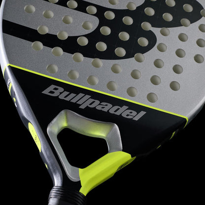 Close-up of the Bullpadel Indiga Ctr 2026 Padel Racket by Bullpadel, showcasing its silver and black face with round holes and yellow accents, crafted for precision control against a sleek black background.