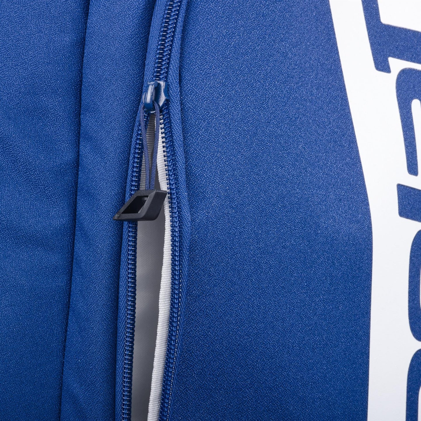 Close-up of the Babolat Court Hero Padel Backpack in dark blue, made from recycled PET. The partially open zipper with a black pull is visible, along with partial white Babolat branding on the right side.