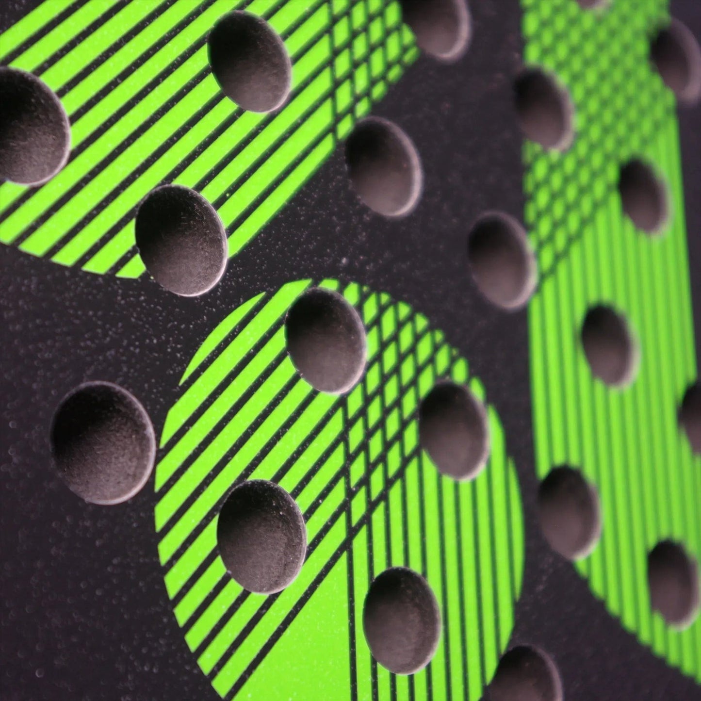 Close-up of the Karakal Air Lite 345 Green Padel Racket by Karakal, highlighting its black surface with raised circular bumps and bright green diagonal patterns intersecting at different angles.