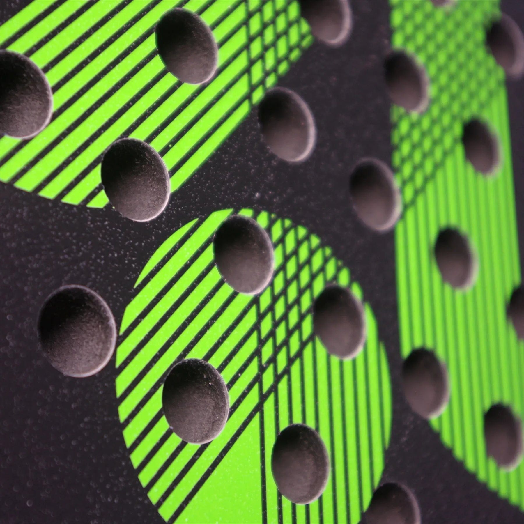 Close-up of the Karakal Air Lite 345 Green Padel Racket by Karakal, highlighting its black surface with raised circular bumps and bright green diagonal patterns intersecting at different angles.