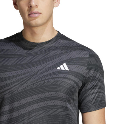 An individual wears an adidas Club Men's Graphic Padel T-Shirt - Black, showcasing a white logo on the chest. Made from recycled materials and featuring AEROREADY technology, the image focuses on the upper torso and parts of the face, with a neutral expression.