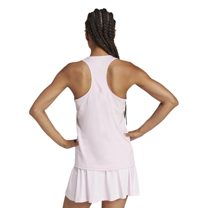 A person with long braided hair stands with hands on hips, seen from the back in a light pink ADIDAS Womens Club Padel Tank Top and skirt ensemble made from recycled materials.