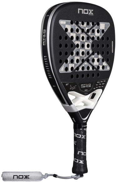The NOX Luxury AT10 Genius Attack 18K Alum By Agustin Tapia 2026 Padel Racket features a black and silver design, 18K aluminised carbon, large "X" graphic, perforated holes, and a wrapped handle with attached white wrist strap.