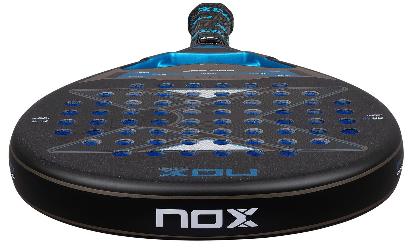 A close-up of the NOX AT10 Pro Cup Soft By Agustín Tapia 2026 Padel Racket shows its perforated black surface with blue accents, the NOX logo, and a handle inspired by Agustín Tapia.