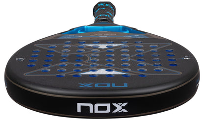 A close-up of the NOX AT10 Pro Cup Soft By Agustín Tapia 2026 Padel Racket shows its perforated black surface with blue accents, the NOX logo, and a handle inspired by Agustín Tapia.