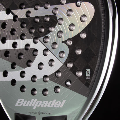 Close-up of the Bullpadel HACK 04 2026 Padel Racket in Black/Grey, highlighting its textured face with round indentations and bold Bullpadel logo. Sharp lighting accentuates its dynamic power and refined design.