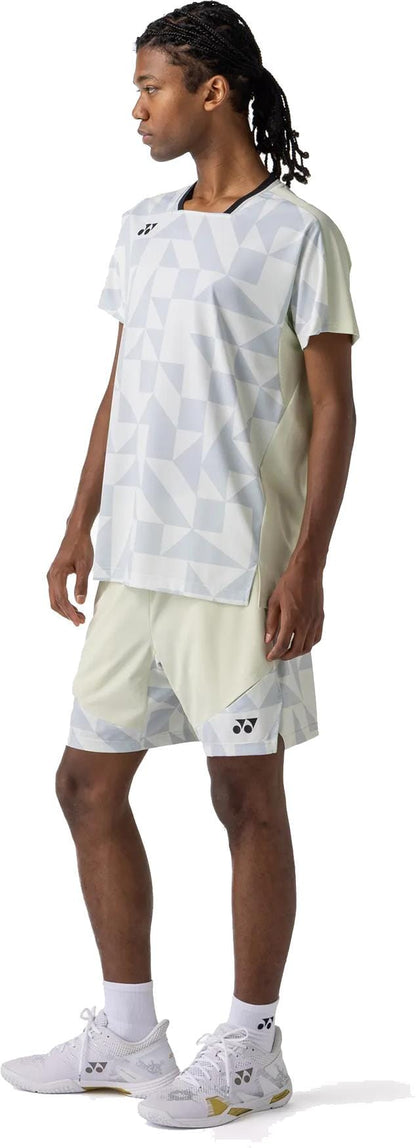 A person with long braids wears the Yonex 10712YX Crew Neck Mens Padel T-Shirt in Champagne, paired with matching shorts, white socks, and white athletic shoes, standing sideways against a white background.
