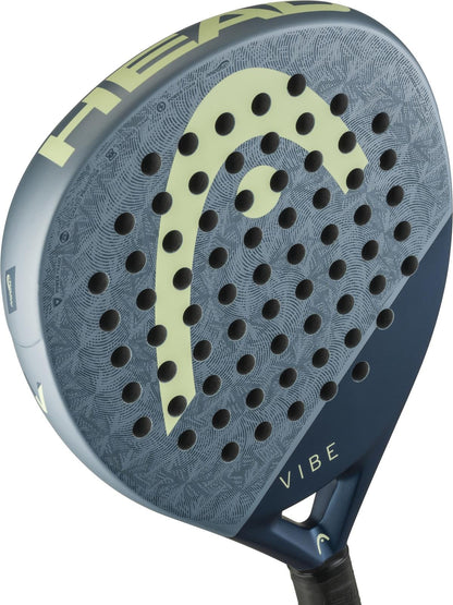 A close-up of the HEAD Vibe 2026 Blue / Yellow Padel Racket by HEAD, showcasing its blue and grey patterned fibreglass surface with circular holes, the light yellow HEAD logo, and "VIBE" near the handle.