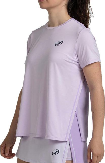 A woman wears the Bullpadel Picase Women’s Padel T-Shirt in pastel lilac with black logos, paired with a matching skirt. Her hair is pulled back and her face is partially out of frame, highlighting stylish Bullpadel performance apparel.