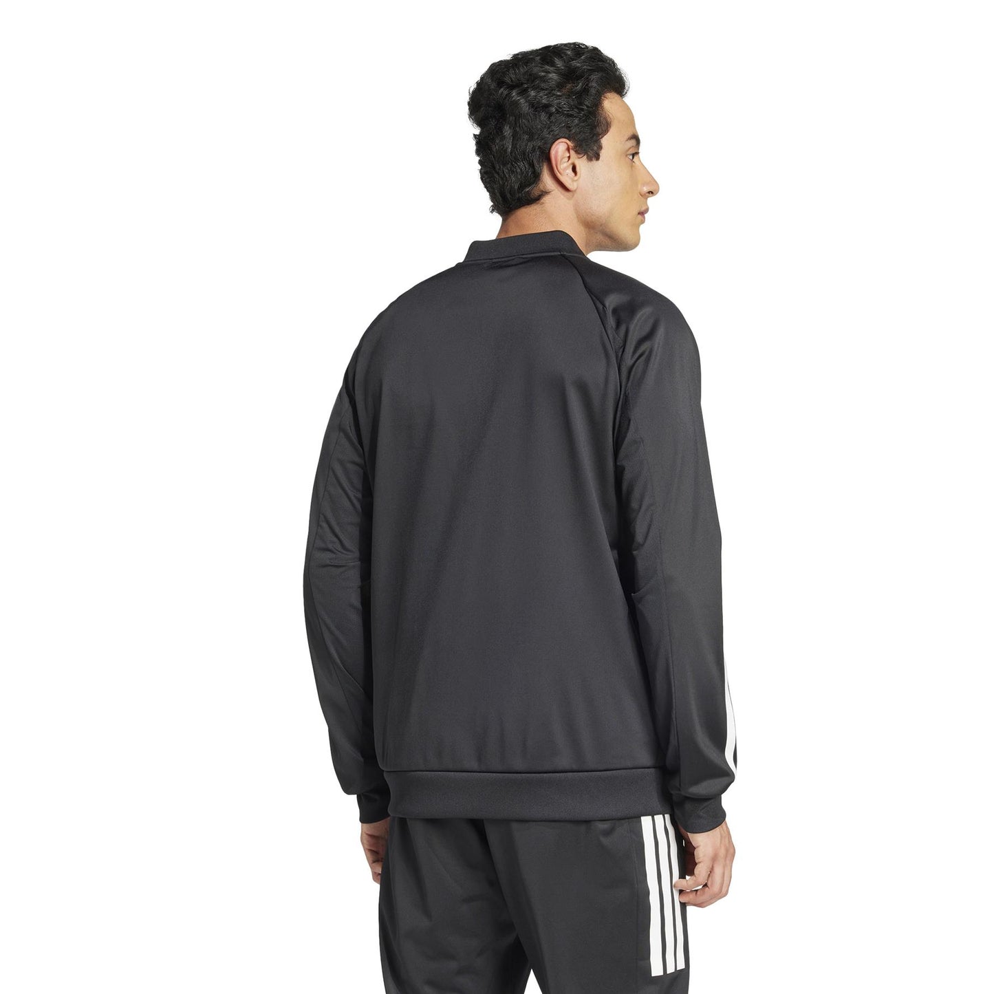 A person with short dark hair wears the adidas Men's 3 Stripe Knit Padel Jacket in Black, featuring the iconic striped sleeves, paired with matching pants. They stand against a plain white background, looking to the side.