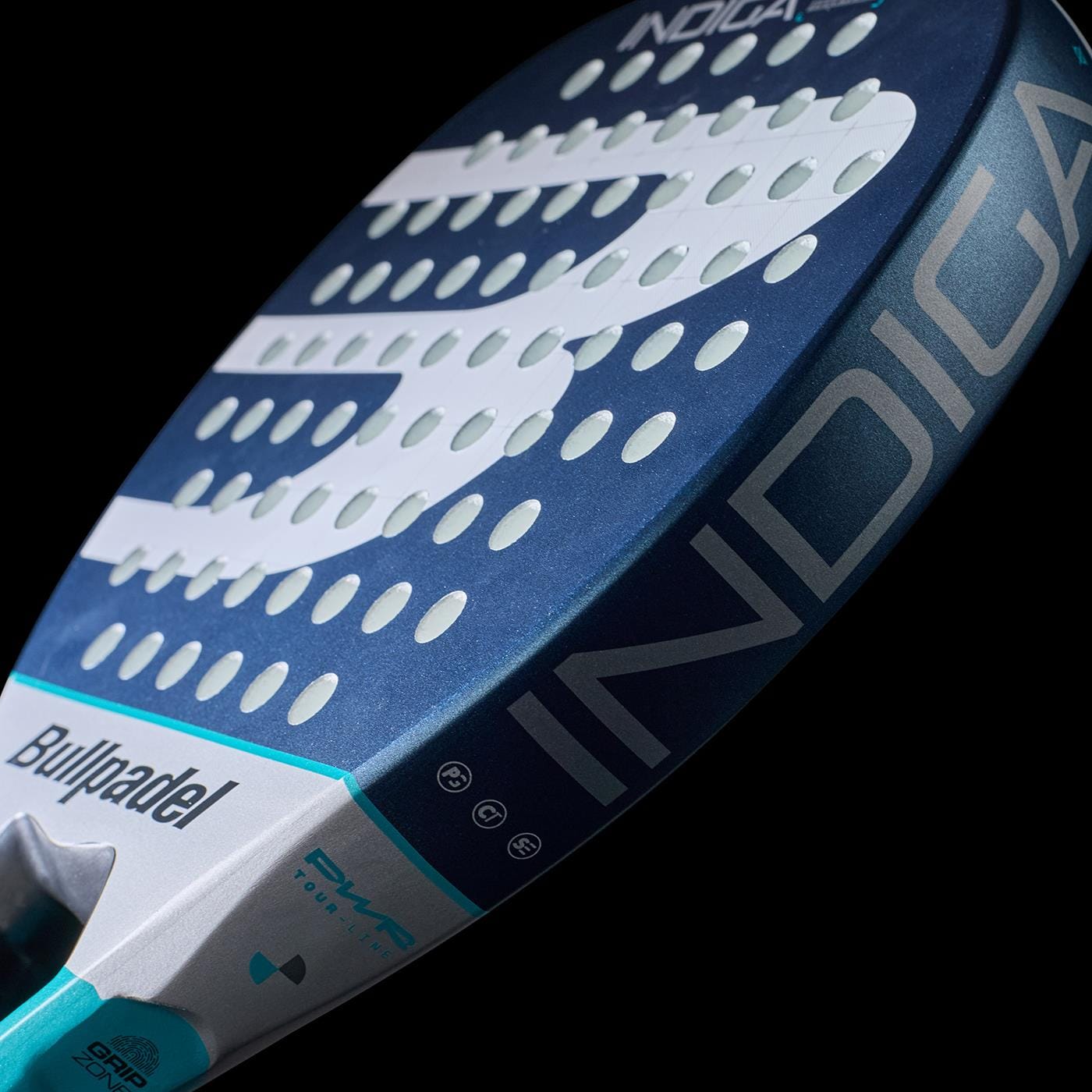 Close-up of the Bullpadel Indiga Pwr 2026 padel racket by Bullpadel, in blue and silver with "INDIGA" on the side, white geometric designs on black, and circular holes—engineered for power and performance.