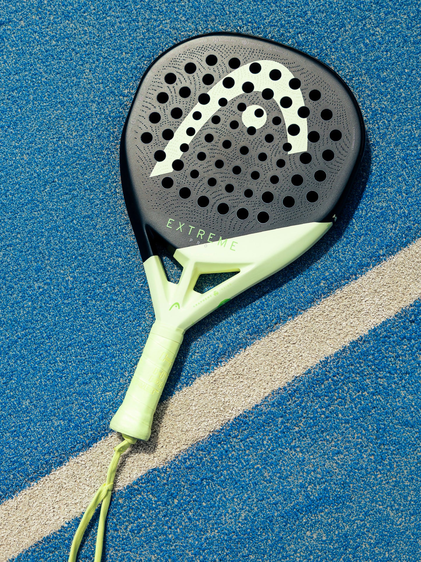 A black and green HEAD Extreme Pro 2026 Padel Racket, featuring the word “EXTREME” on its surface, rests on a blue textured court beside a white line—making it the ideal choice for advanced padel players looking for a powerful racket from HEAD.