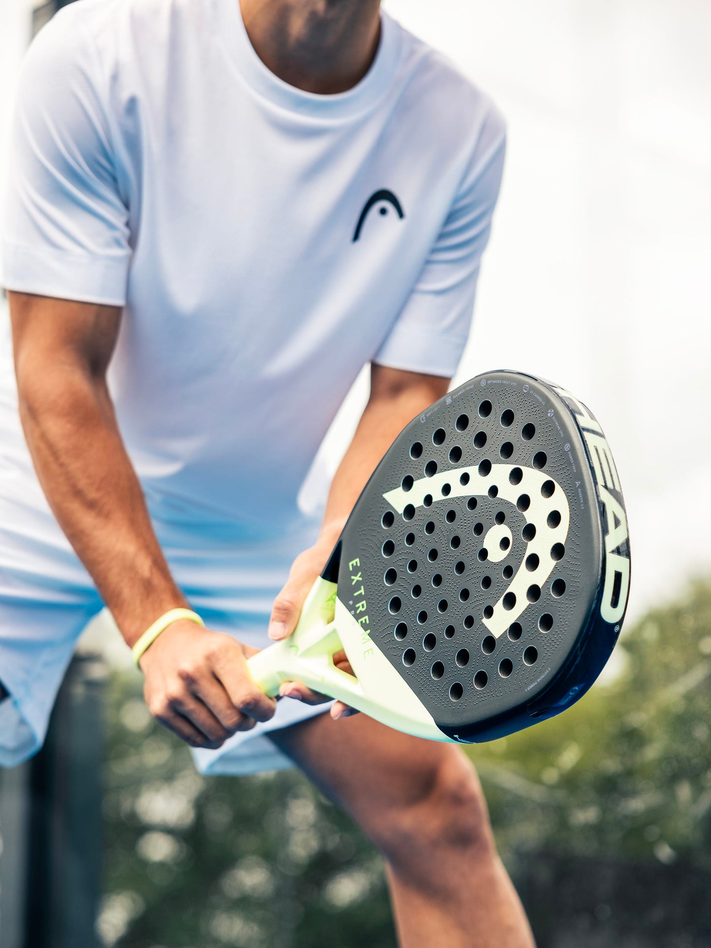 A person in a white shirt and shorts holds the HEAD Extreme Pro 2026 Padel Racket—a black and yellow power padel racket from HEAD—poised to play. The image highlights the player’s arms and the racket, showcasing equipment crafted for advanced padel players.