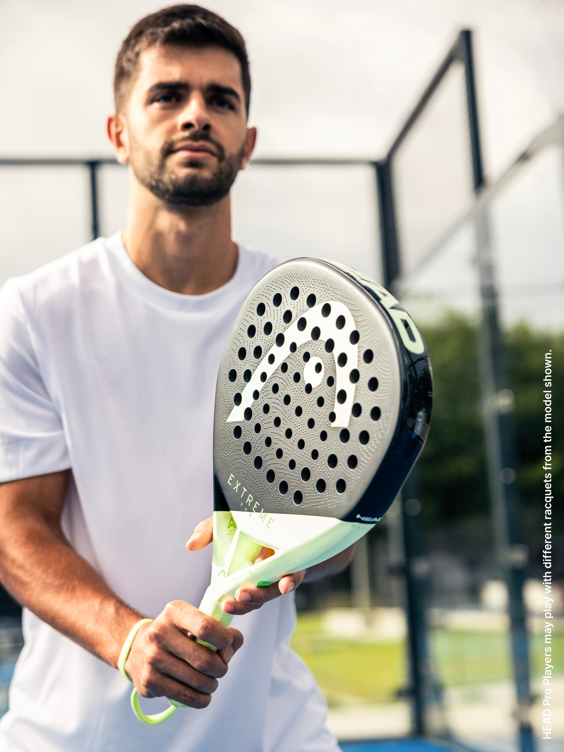 A man in a white shirt grips the HEAD Extreme Pro 2026 Padel Racket, standing poised on an outdoor court with determination—an image that showcases the intensity and power experienced by advanced padel players using a top-tier HEAD racket.