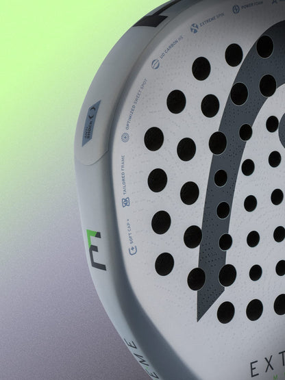 Close-up of the HEAD Extreme Motion 2026 Padel Racket against a gradient background, showcasing its perforated surface, technical icons, and HEAD logo details on the racket’s edge—expertly crafted for advanced padel players in search of a true power padel racket.
