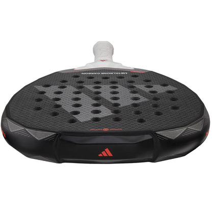 Close-up of the adidas Metalbone Carbon 3.4 Padel Racket in black/white, showcasing its textured surface with holes. Designed for advanced players, it has a white grip handle and features red accents and a logo on the edge.